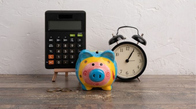 A Calculator, Piggy Bank And Clock On A Desk Indicating Simplified Tax Reporting