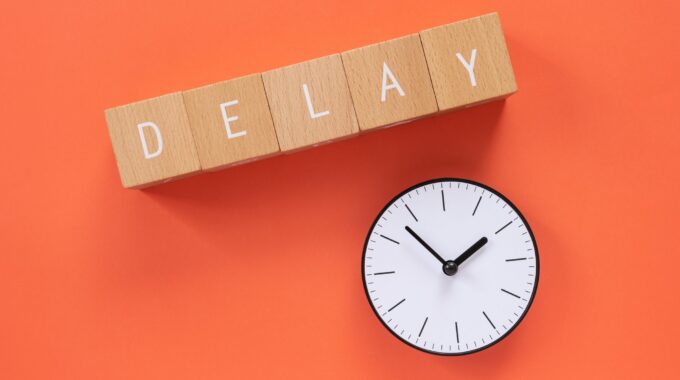 Delay; Five Wooden Blocks With "DELAY" Text Of Concept And A Simple Clock.