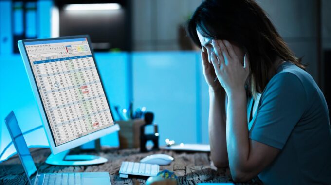 Woman With Head In Hands At Computer Trying To Sort Accounting Errors